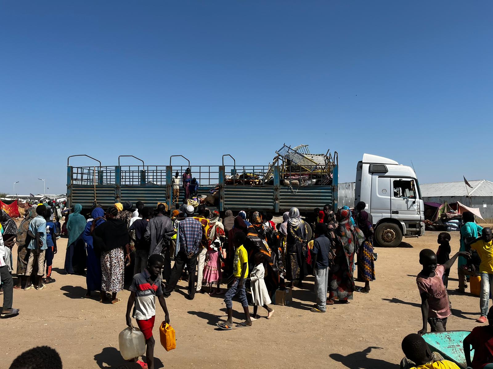 People get out of a truck that brought them from the border with Sudan to the transit center in Renk, South Sudan; just a few suitcases and bed railings can be seen.