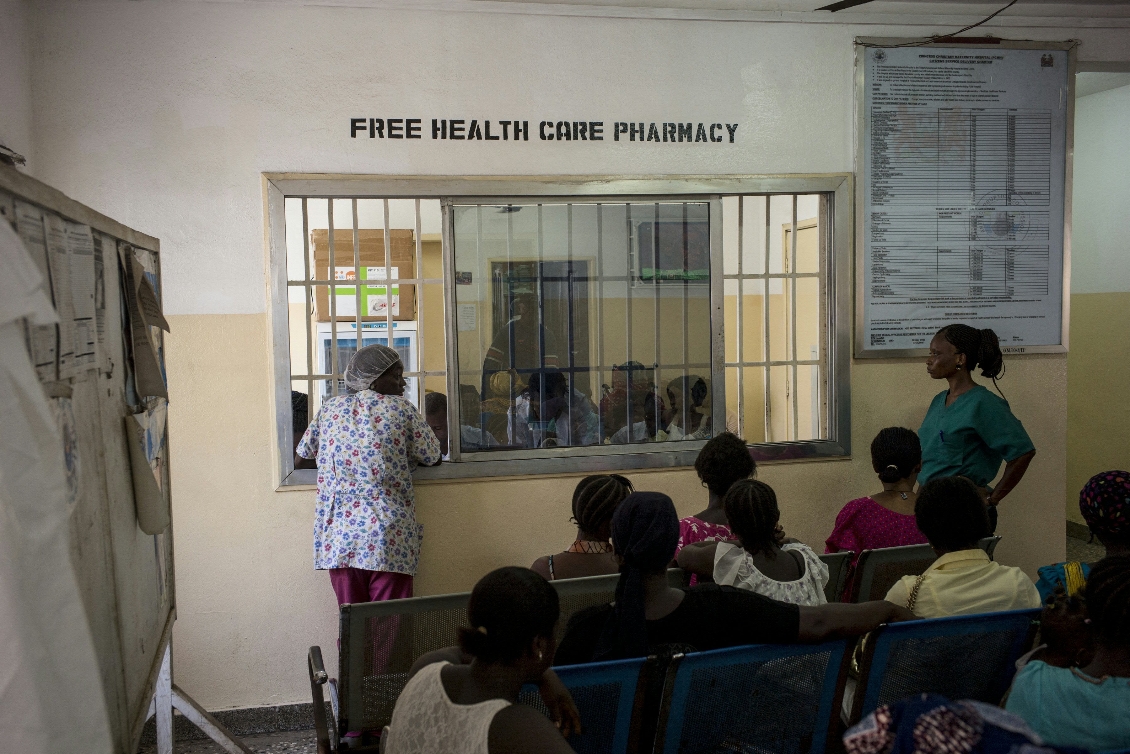 Women sit in a waiting area of a hospital near the window for a "free health care pharmacy"