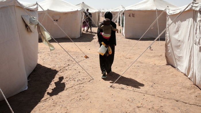 A Sudanese woman displaced from El-Fasher carries her child as she walks between tents at El-Afadh camp in Al Dabbah, in Sudan's Northern State, November 16, 2025. 