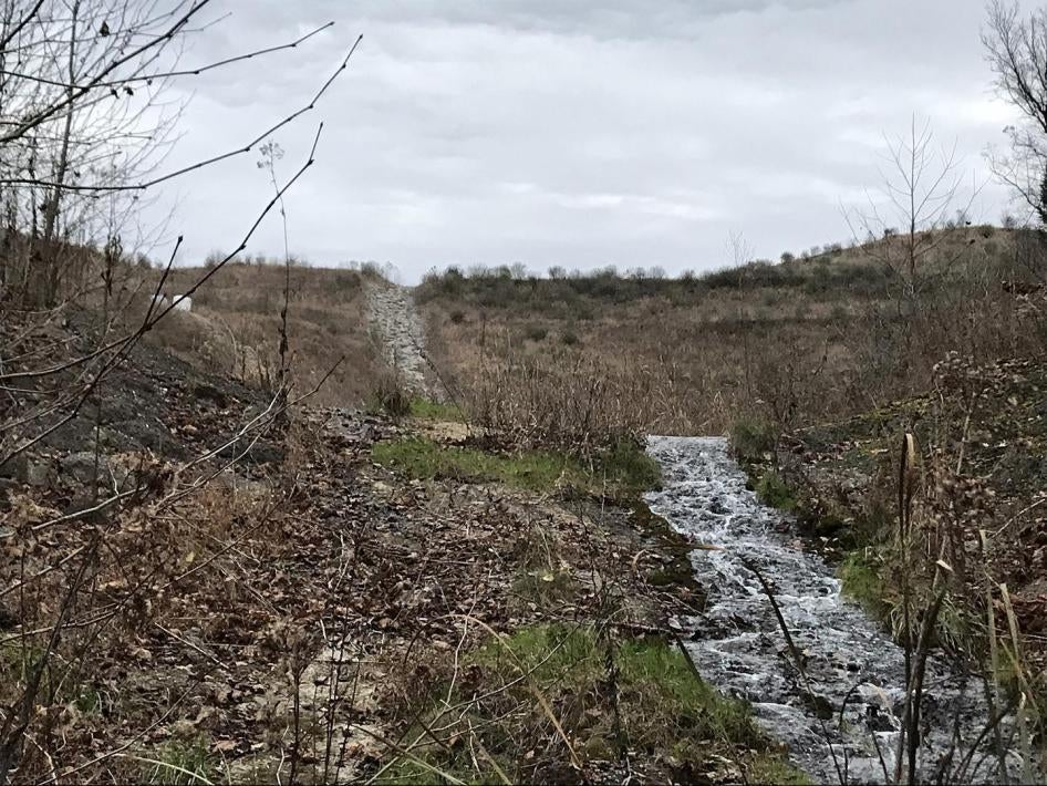 A valley fill with rocks replacing the buried streambed in the background and the surviving stream in the foreground